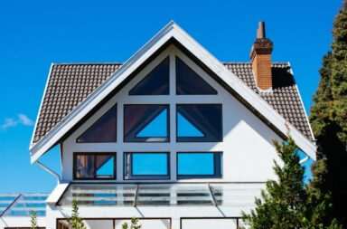 A modern A-frame house with large windows against a clear blue sky, showcasing contemporary architecture.